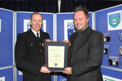 Carl award The image shows Carl, a man with a beard, receiving a commendation for his work in the Thames Valley Police control room. He is smiling and holding a framed certificate while standing next to a police officer in uniform.